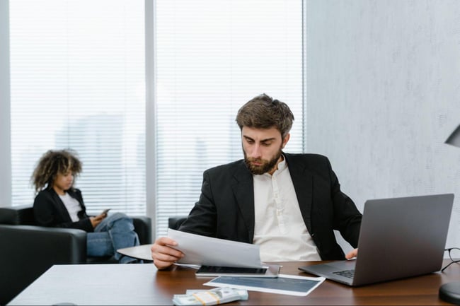 Finance professional reviewing printed reports alongside compliance management software on laptop