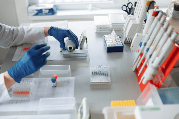 Pharmaceutical lab technician handling samples and manually recording data, reflecting compliance workflows managed through paper-based processes.
