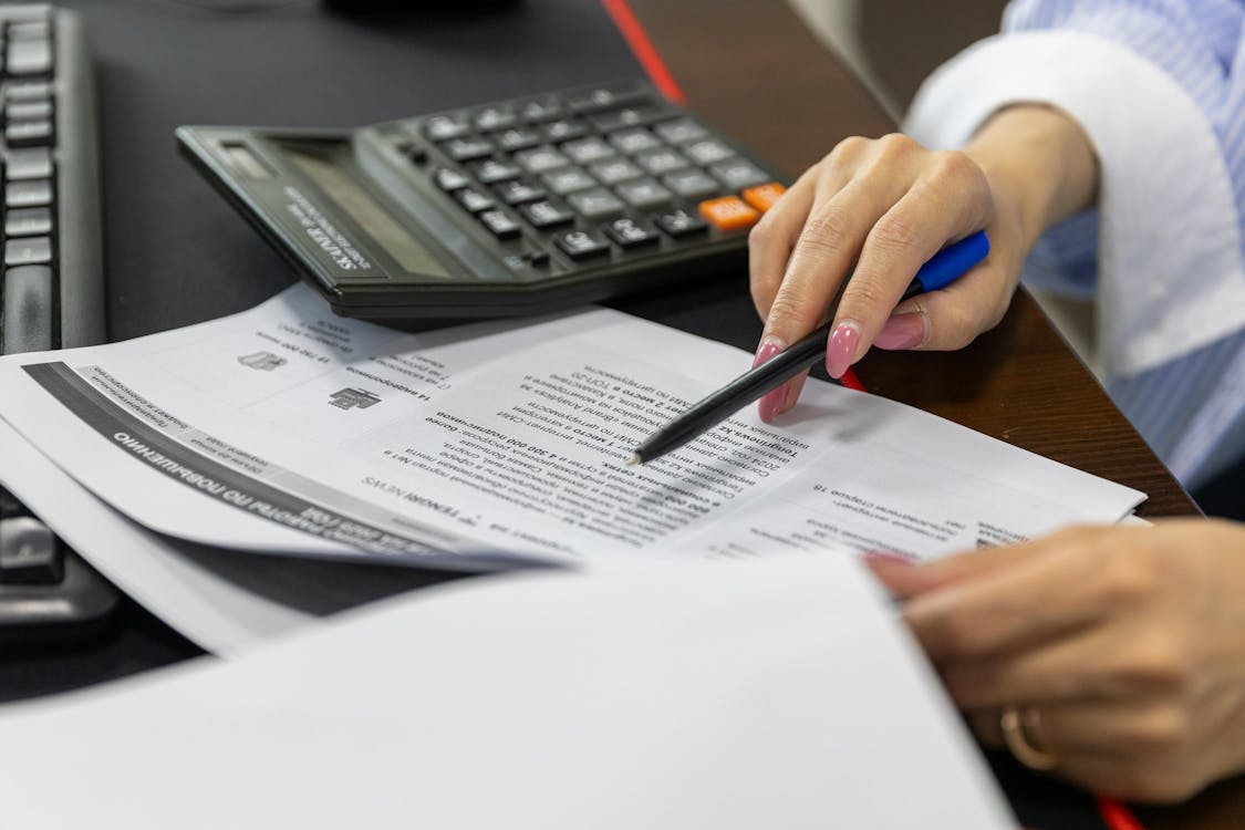 Quality professional reviewing printed compliance documents with a pen and calculator, highlighting the inconvenience of manual documentation and record-keeping in FDA-regulated environments.
