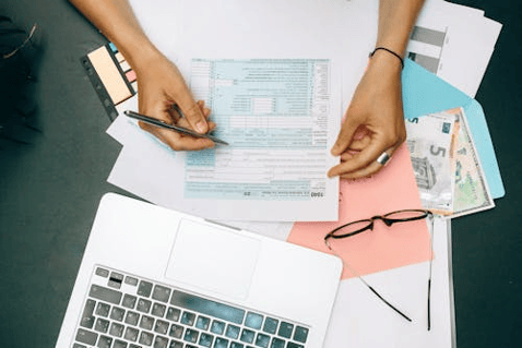 Employee completing workplace compliance training on a laptop at a desk with documents, a notepad, and eyeglasses.